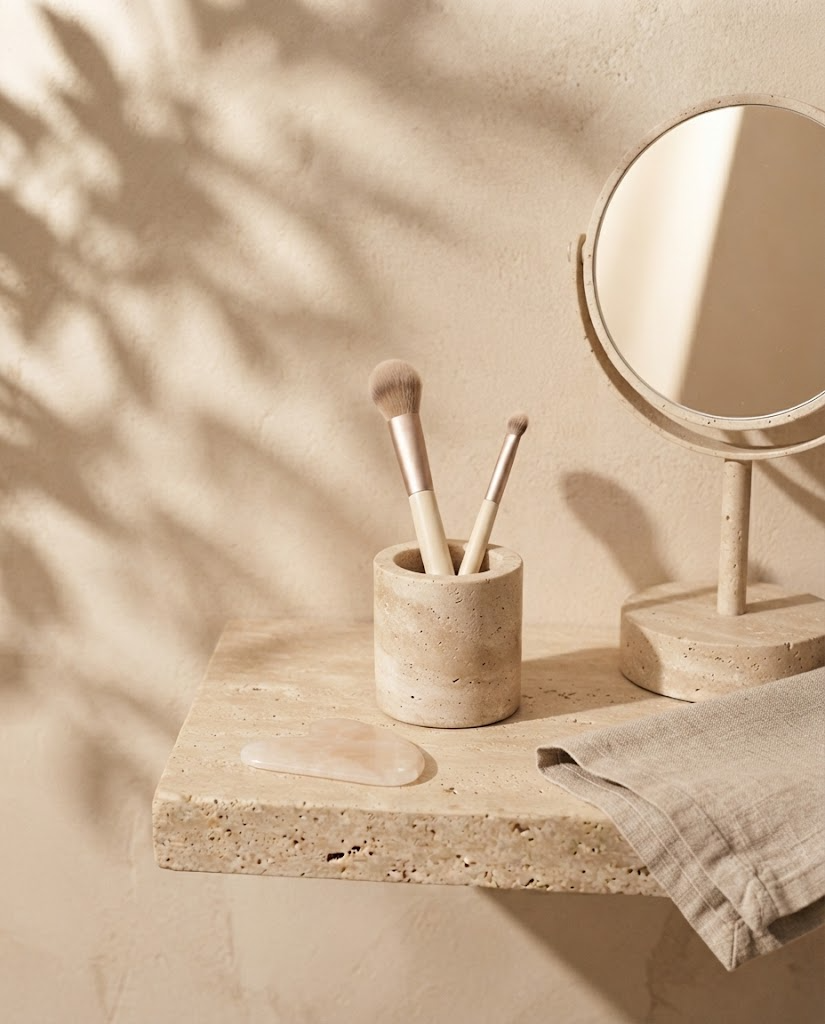 Stilleven met make-upkwasten, spiegel en gua sha op travertin